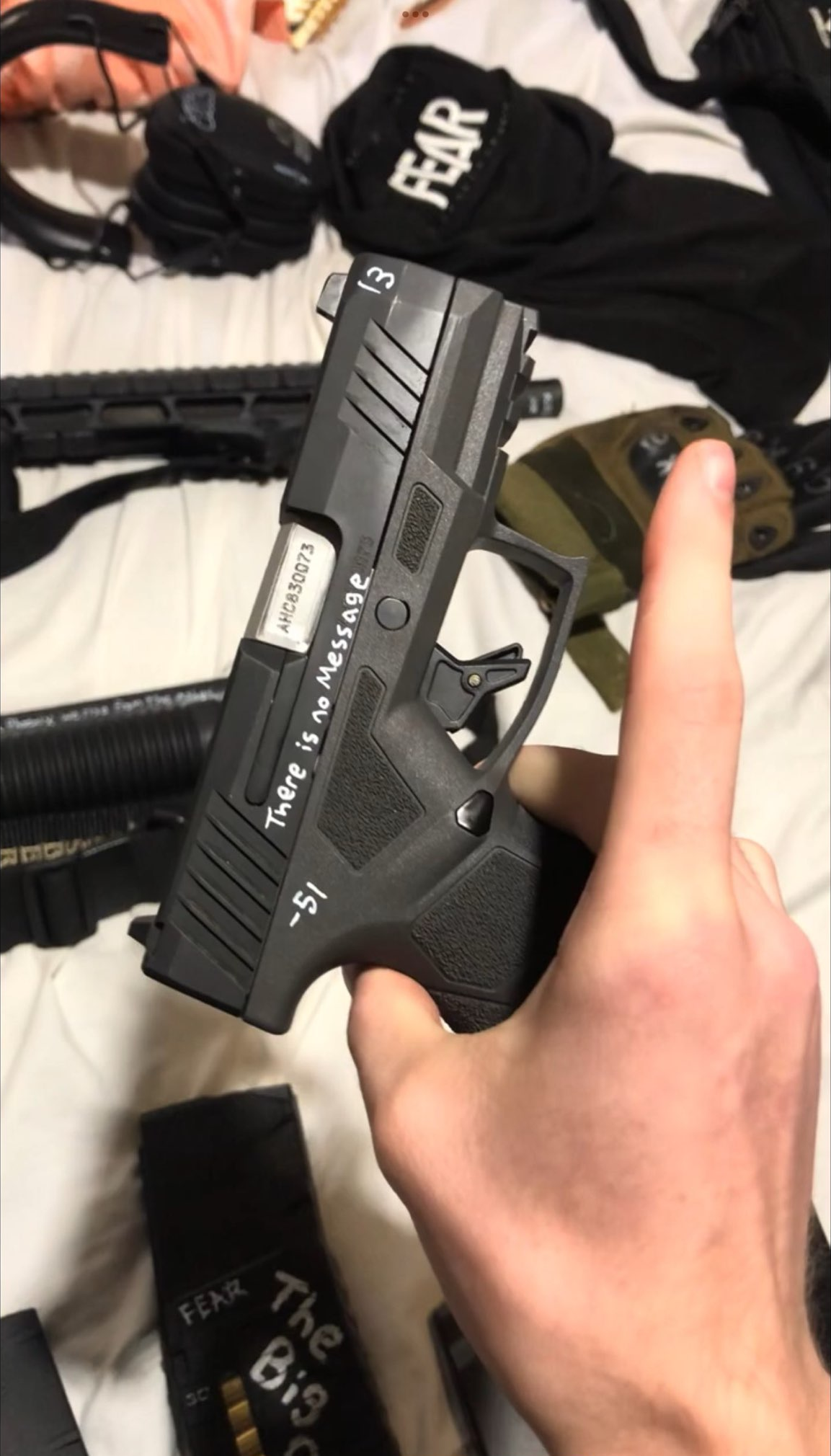 The attacker's hand holding a handgun, upon which they wrote "There is no message" and "-51." Another firearm is visible in the background as well as a magazine with white writing on it that say "fear" and "The Big..."