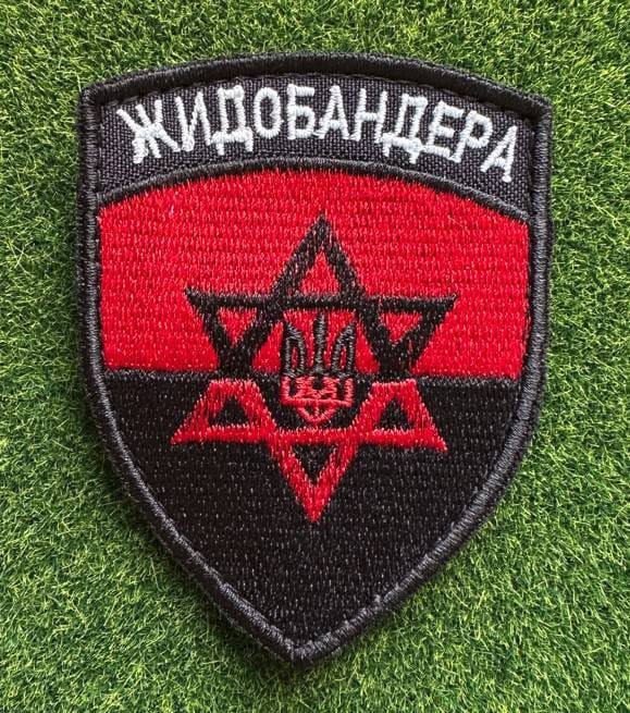 Fabric patch of a Ukraine trident inside a Star of David inside a Banderite flag. The flag is which is red on top and black on the bottom. The patch is shaped like a shield.