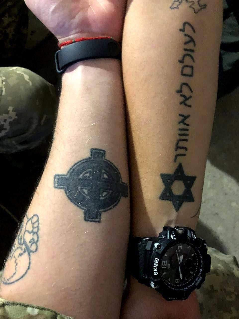 Two arms cross to compare their tattoos: a Third Waffen Division Totenkopf and a Neo-Nazi Crosshair or Celtic Cross on one, a Star of David and Hebrew text on the other. 